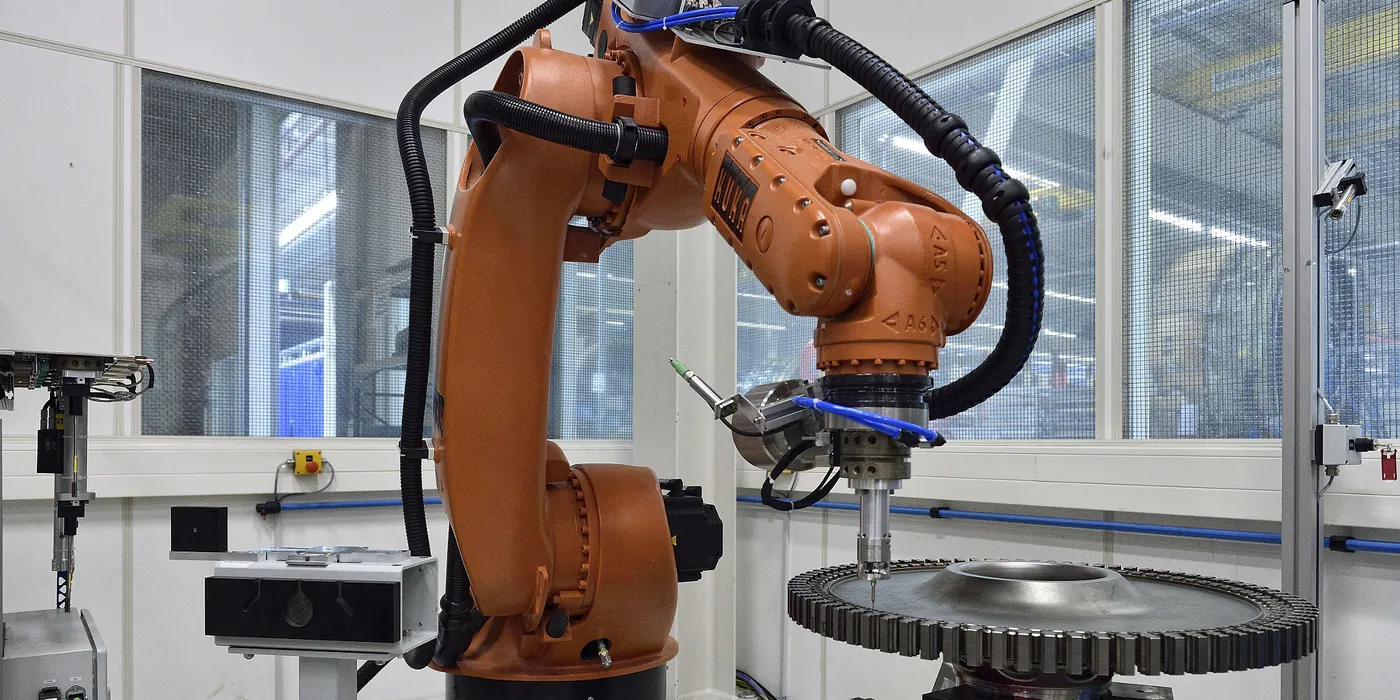 Orange industrirobot der bearbejder et stort tandhjul i en lys, moderne robotcelle