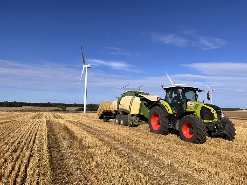 Claas Axion med Krone BiG Pack på stubmarken under en stor himmel