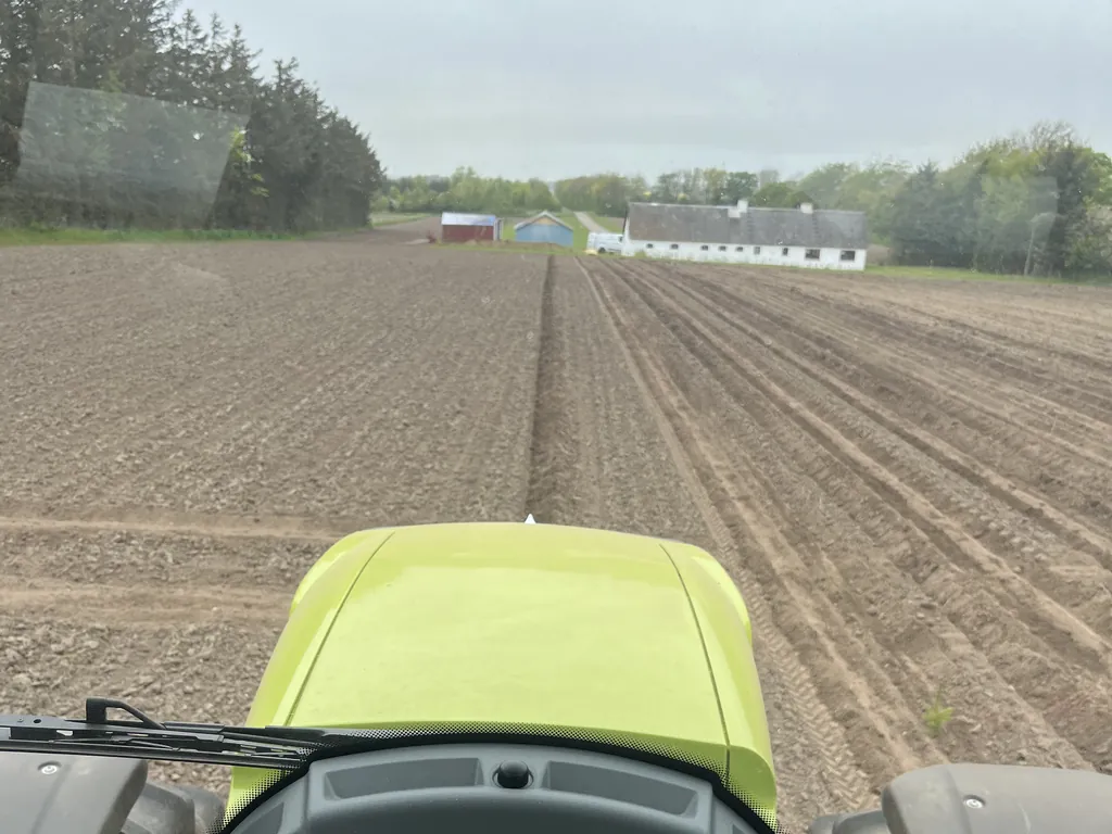 Udsigt fra traktoren ud over en nyplantet mark med plantefurer